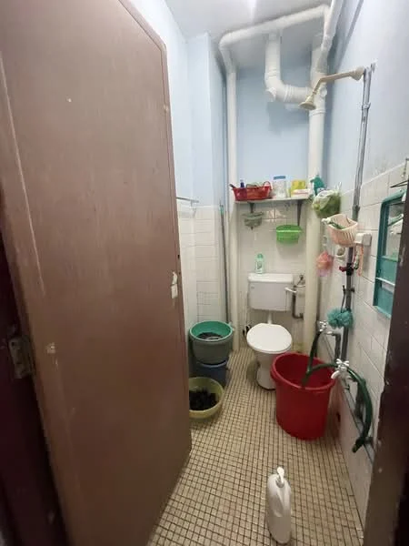 Bathroom features: white toilet, sink with chrome faucet, green plastic storage baskets, red plastic bucket, blue plastic bucket, cleaning supplies, tiled flooring, white tiled walls, exposed plumbing, hanging storage rack.