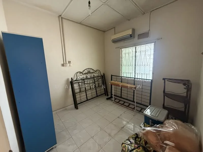 Room features: white painted walls, tile flooring, window with metal grille, wall-mounted air conditioning unit, metal bed frame, wooden shelving unit, folding table, blue wardrobe, cooler, plastic wrapping on furniture.