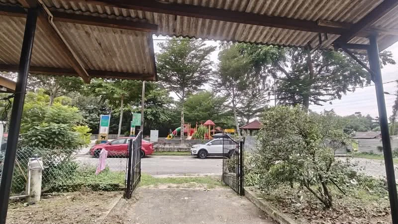 Exterior features: gate entrance, fenced yard, manicured shrubs, playground visible in background, paved walkway, roadside view, surrounded by greenery, open space.