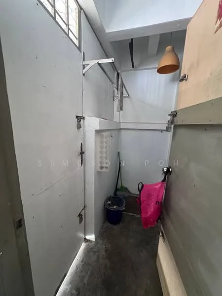 Room features: grey concrete flooring, white painted walls, exposed ceiling, hanging light fixture, metal shelving unit, bucket, pink bag, window for natural light.