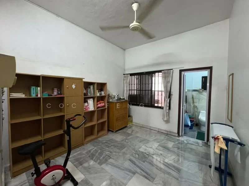 Room features: white painted walls, marble flooring, ceiling fan, window with black metal grille, wooden bookshelf, wooden cabinet, exercise bike, laundry rack, door leading to bathroom, green carpet in bathroom area.