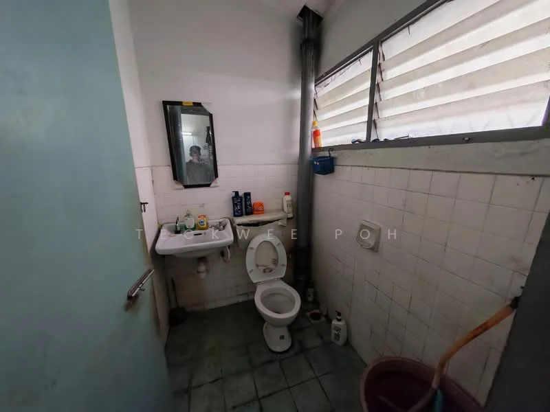Bathroom features: white tiled walls, grey tiled flooring, toilet, sink with mirror, window with horizontal slats, toilet paper holder, cleaning supplies, broom.