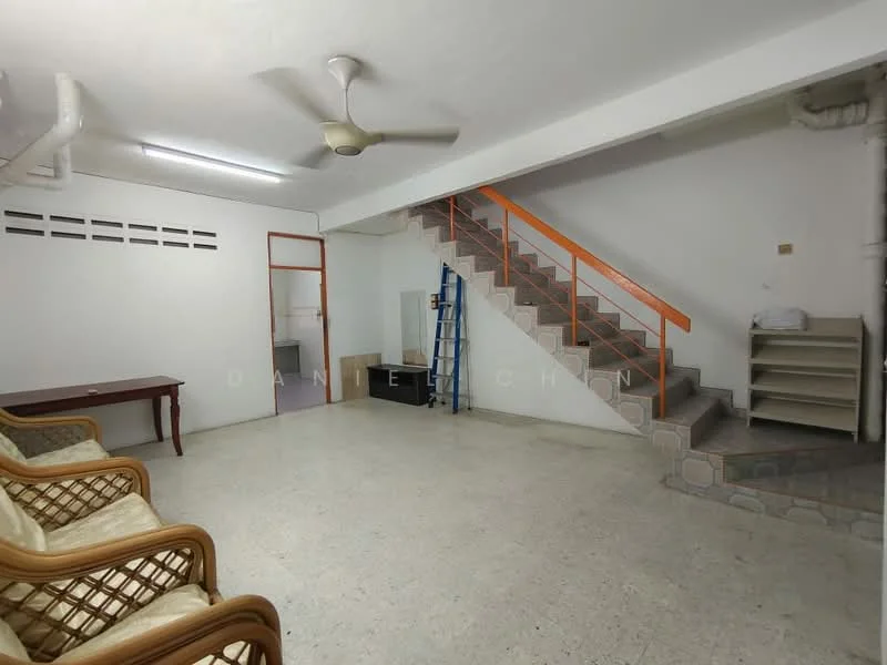 Living features: white painted walls, concrete flooring, 5-blade ceiling fan, wooden dining table, rattan armchairs, staircase with orange railing, built-in shelving unit, window with ventilation grilles.