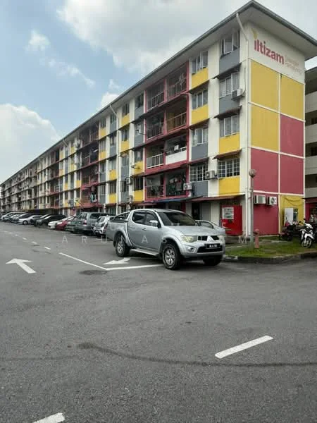 Exterior type: low-rise apartment block; features: yellow and red painted facade, multiple floors, balconies with railings, air conditioning units visible, parking lot in front, cars parked along the street, sidewalk, street lighting, surrounding greenery; style: modern.