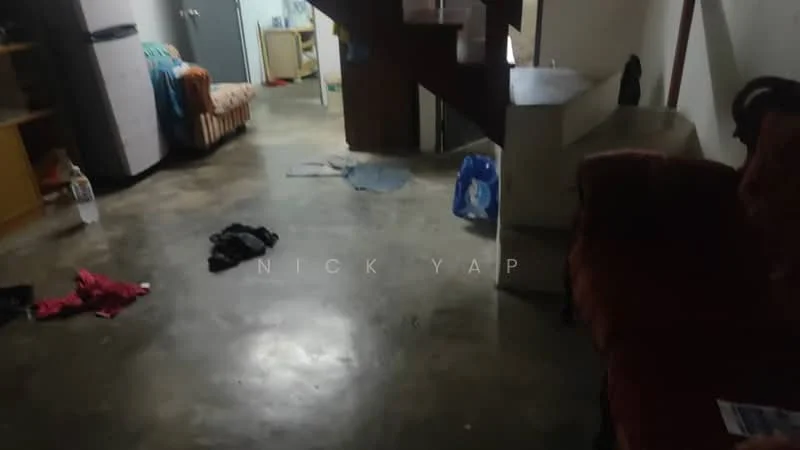 Room features: concrete flooring, staircase with wooden handrail, sofa in red fabric, small table, refrigerator, striped sofa, clothes on the floor, open space layout.