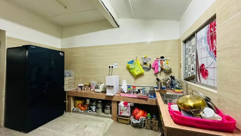 Kitchen features: black fridge, stainless-steel sink, chrome faucet, countertop with beige surface, wooden cabinetry, open shelving, kitchen utensils hanging on wall, various containers and appliances on countertop, tile backsplash, window with decorative grille.