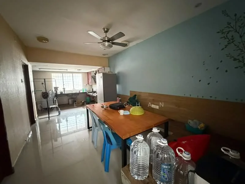Dining features: wood dining table, blue plastic chairs, ceiling fan with light, white walls, light-colored tiled flooring, decorative wall with tree design, water bottles on table, kitchen area visible in background; style: modern. Kitchen features: stainless-steel fridge, kitchen cabinets, sink, countertop, kitchen appliances visible; style: modern.
