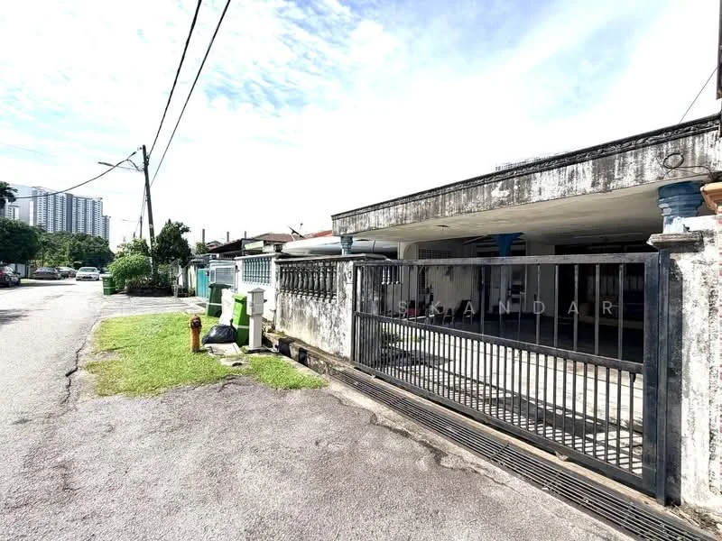 Exterior type: detached bungalow; features: concrete facade with weathered finish, gated entrance with metal gate, single-storey structure, manicured lawn, paved driveway, surrounded by greenery, visible street view, adjacent to residential area; style: traditional.