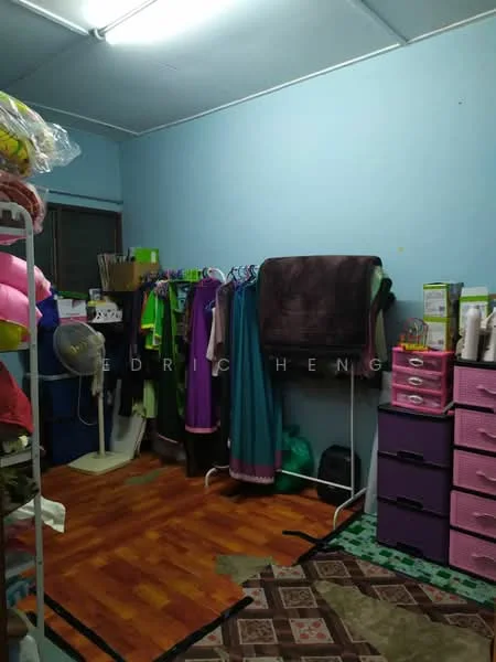 Room features: blue painted walls, wood laminate flooring, clothes rack with hangers, folded blankets, fan, pink storage drawers, area rug with geometric pattern, window with curtain, clothes hanging on rack.