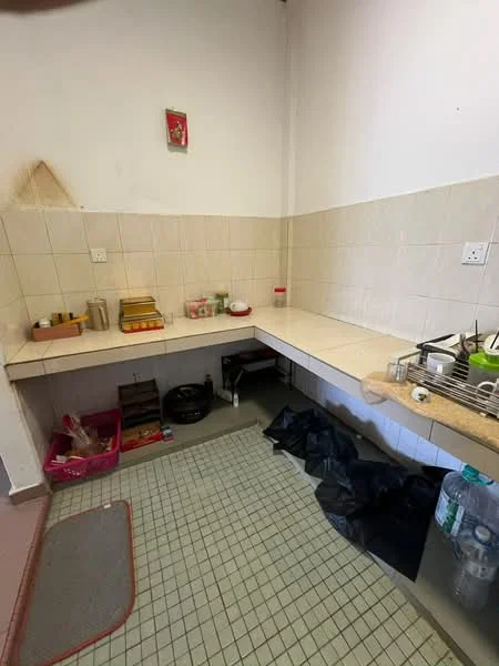 Kitchen features: white tiled walls, light-colored countertop, sink with faucet, wall-mounted shelves, floor tiles in green and white pattern, open storage space, plastic storage bins, cleaning supplies, kitchen utensils, dish rack.
