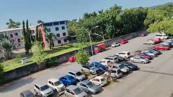 Exterior type: low-rise apartment block; features: manicured lawn, mature trees, parking lot with multiple vehicles, surrounded by greenery, two-storey building, red and white facade, fenced perimeter; style: modern.