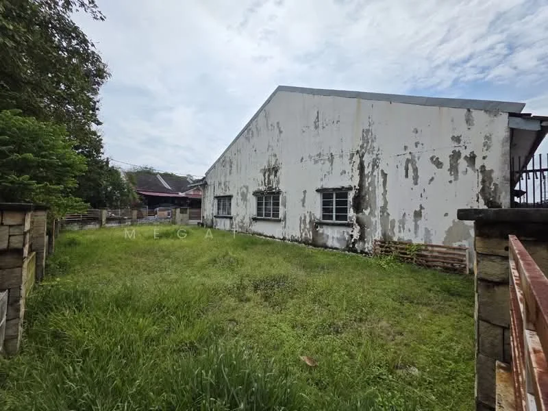 Exterior features: weathered exterior walls, multiple windows, overgrown grass, surrounding greenery, fenced perimeter, single-storey structure, asymmetrical roof.