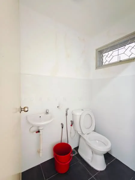 Bathroom features: white painted walls, black tile flooring, one-piece toilet, wall-mounted sink, exposed plumbing, window with decorative grille, red bucket.