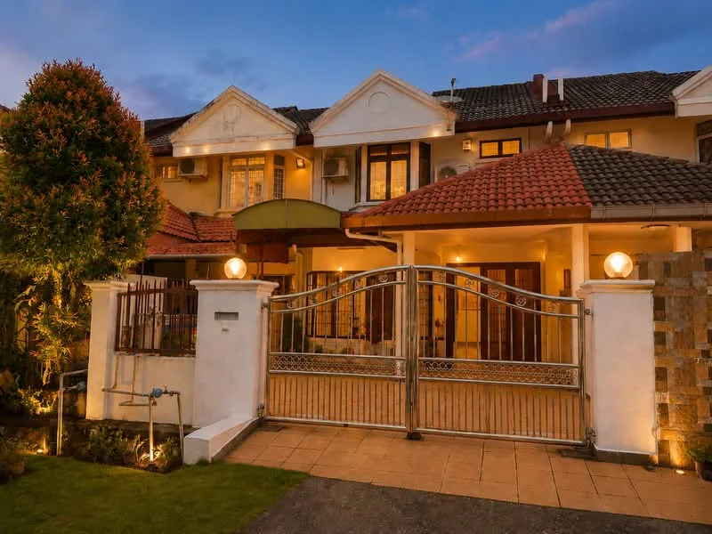 Exterior type: linked terrace house; features: gated entrance, stone cladding on wall, tiled walkway, manicured landscaping, outdoor lighting, double-storey facade, red tiled roof, cream painted facade, decorative columns, front porch with awning; style: modern.