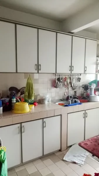 Kitchen features: white cabinetry with silver handles, ceramic tile backsplash, double-bowl stainless-steel sink, chrome pull-down faucet, countertop with beige surface, various kitchen utensils and containers, dish rack, colorful plastic bowls, cleaning supplies, floor tiles in light color.