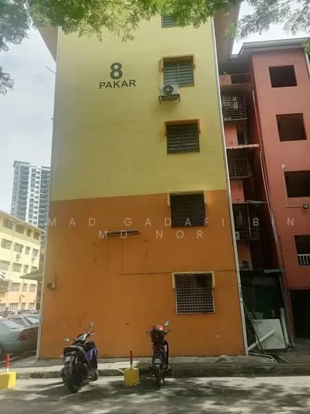 Exterior type: low-rise apartment block; features: orange painted facade, cream painted facade, multiple windows with grilles, air conditioning unit visible, number '8' displayed on the building, parking area with motorcycles, surrounding greenery, adjacent buildings visible; style: traditional.