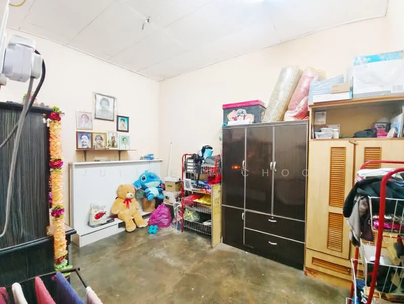 Room features: painted walls in light color, concrete flooring, ceiling with fluorescent lighting, wooden wardrobe with sliding doors, black storage cabinet, shelves with various items, stuffed teddy bear, decorative items on wall, baskets for storage, folded blankets or towels.