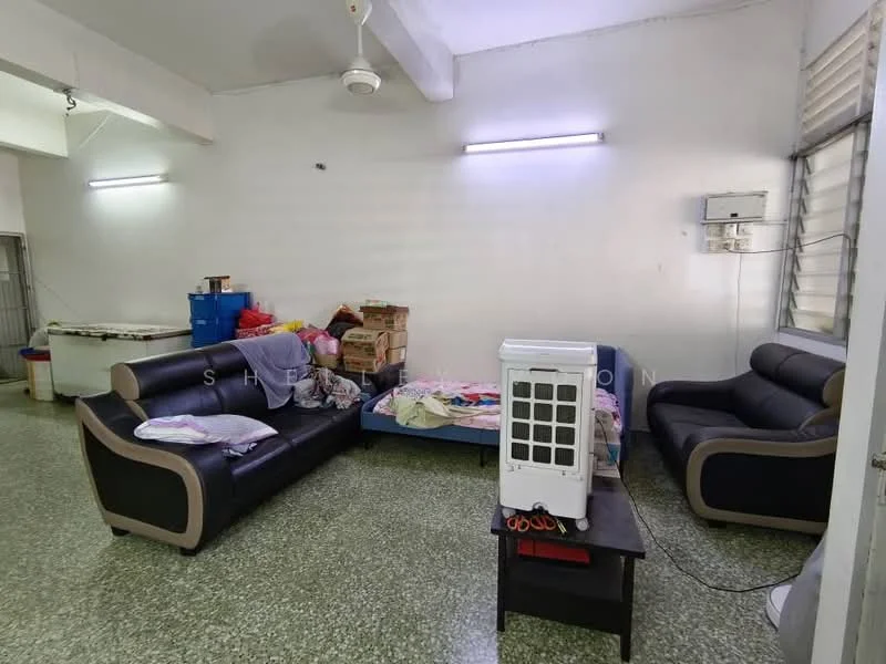 Living features: 2-seater leather sofa in black, 3-seater fabric sofa in grey, coffee table, green terrazzo flooring, white painted walls, ceiling fan, wall-mounted air conditioning unit, window with blinds, decorative items on the sofa, boxes and clutter in the background.