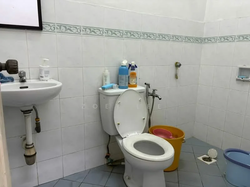 Bathroom features: white tiled walls, blue floor tiles, single-sink vanity, toilet, handheld shower, wall-mounted faucet, soap dispenser, cleaning supplies, bucket, drain, toilet paper holder.