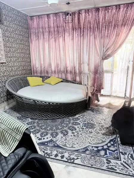 Living features: round wicker daybed with white cushion, two yellow accent pillows, pink curtains with palm leaf pattern, decorative wallpaper with floral pattern, area rug with intricate design, ceiling fan, sliding glass door, wooden flooring; style: modern.