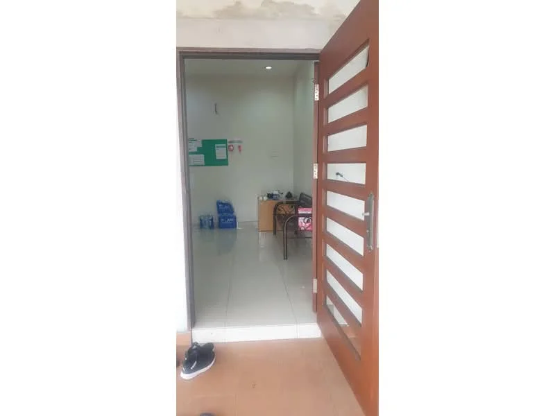 Room features: brown wooden door with horizontal slats, white walls, glossy tile flooring, recessed lighting, table with chairs, green bulletin board, plastic water bottles, empty space, shoes on the floor; style: modern.