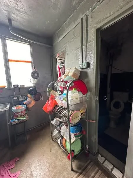 Laundry features: grey painted walls, concrete flooring, metal shelving unit with dishes, hanging clothes, sink, window with orange curtains, doorway leading to bathroom, toilet visible in adjacent room.