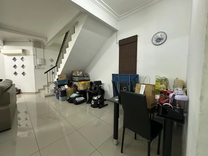 Room features: white painted walls, tile flooring, staircase with black railing, sofa in light grey, dining table with black chairs, various boxes and bags stacked, air conditioning unit on wall, window with brown blinds, decorative wall clock; style: modern.