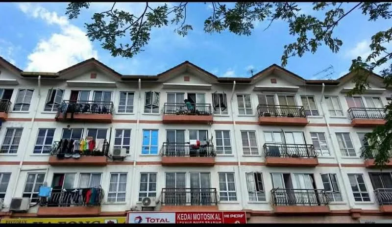 Exterior type: low-rise apartment block; features: white painted facade, red brick accents, balconies with black railings, multiple windows, air conditioning units visible, laundry hanging on balconies, gabled roof, three-storey building, trees in foreground, clear blue sky; style: modern.