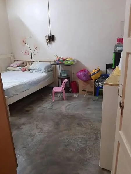 Bedroom features: single bed with light bedding, pink plastic chair, wooden bed frame, concrete flooring, wall with floral decoration, various storage boxes, small table with toys, exposed electrical wiring.