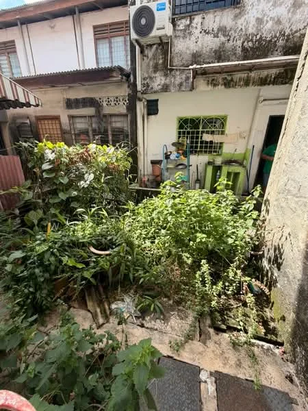 Exterior features: overgrown garden, paved walkway, exposed brick wall, wall-mounted air conditioning unit, greenery including shrubs and plants, fenced area, outdoor storage area, adjacent building structure.