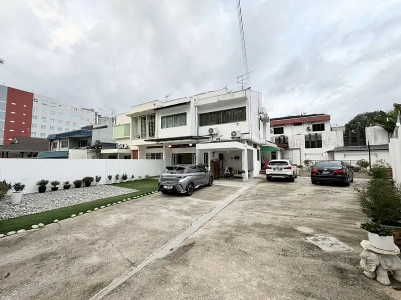 Exterior type: semi-detached house; features: two-storey building, white painted facade, green window shutters, concrete driveway, landscaped garden with pebbled area, parking space for multiple cars, visible air conditioning units, surrounded by low fencing, mature plants in pots, adjacent to a low-rise building; style: modern.