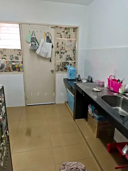 Kitchen features: single-bowl stainless-steel sink, chrome faucet, black countertop, white tiled walls, cream tiled flooring, fridge, wooden cabinet, newspaper wall covering, door to utility area, storage boxes.