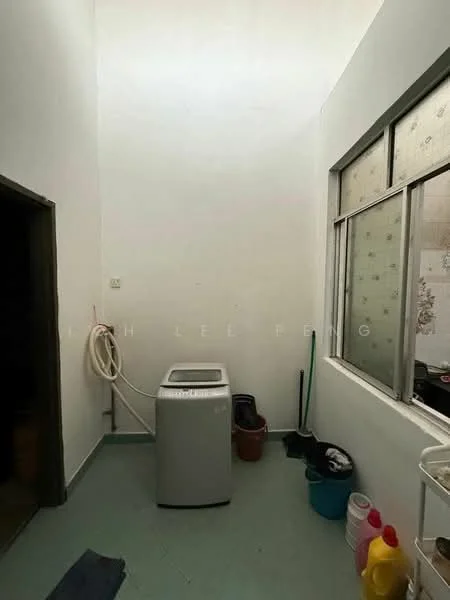 Laundry features: top-load washing machine, white painted walls, green vinyl flooring, window with sheer curtains, cleaning supplies in containers, laundry sink, broom, mop, bucket.