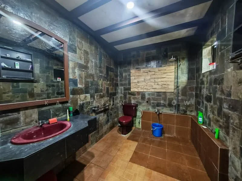 Bathroom features: stone wall cladding, dark wood ceiling beams, brown ceramic tile flooring, red circular sink, chrome faucet, large framed mirror, toilet in dark red, shower area with wall-mounted shower head, tile accent wall behind shower, black countertop, shelf with toiletries, blue plastic bucket; style: modern.