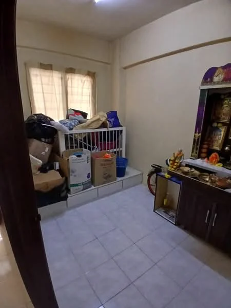 Room features: light-colored painted walls, tile flooring, two windows with sheer curtains, storage boxes, bicycle, small wooden cabinet, decorative altar, various bags and items stacked.