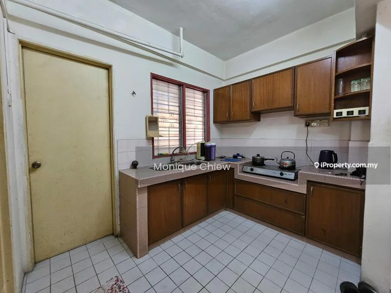 Kitchen features: brown wooden cabinetry, white tiled backsplash, grey countertop, single-bowl stainless-steel sink, chrome faucet, built-in gas stove, freestanding kettle, microwave, window with red curtains, white tiled flooring, wall-mounted shelves.