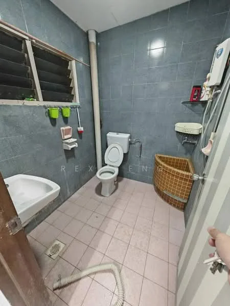 Bathroom features: white toilet, single-sink vanity with white cabinet, chrome basin mixer faucet, grey tiled walls, pink tiled flooring, window with horizontal slats, basket for storage, toilet paper holder, soap dish, drain in floor.