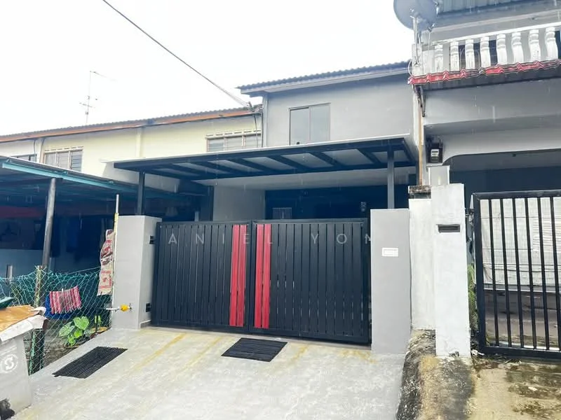 Exterior type: linked terrace house; features: black metal gate with red accents, covered car porch, concrete driveway, grey painted facade, single-storey, front garden area with plants, roof overhang, visible neighboring houses; style: modern.