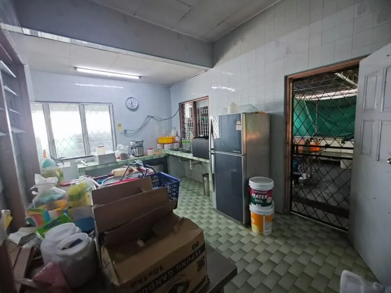 Kitchen features: green tiled flooring, white tiled walls, double-door fridge, stainless-steel sink, wall-mounted clock, window with security grille, kitchen cabinets, countertop workspace, various storage containers, open shelving, doorway to another room.