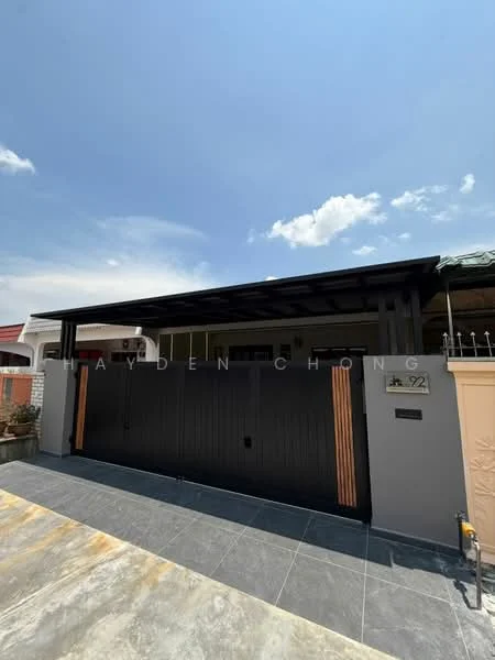 Exterior type: linked terrace house; features: black painted facade, metal gate with wooden accents, flat roof, stone-paved driveway, manicured landscaping, front porch area, intercom panel at entrance, number plaque on wall; style: modern.