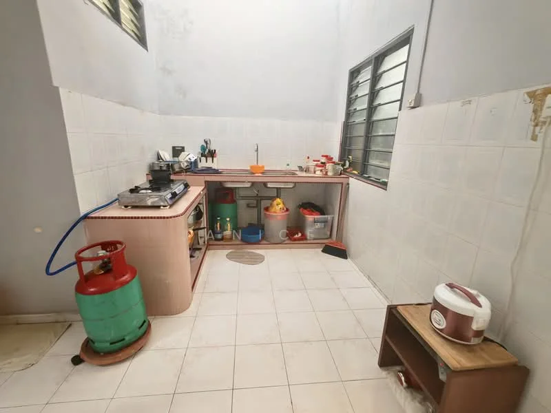 Kitchen features: white tiled walls, light grey painted walls, white tiled flooring, wooden countertop, gas stove, green gas cylinder, sink, kitchen cabinets, plastic storage containers, rice cooker, window with metal grilles, open shelving.