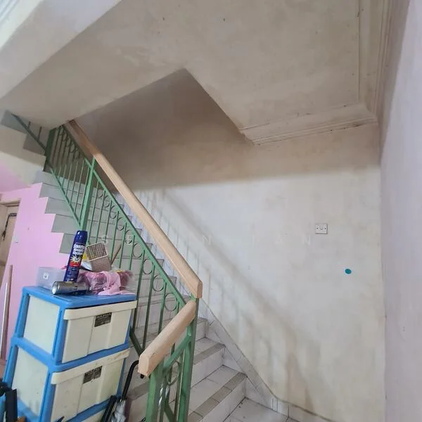 Room features: staircase with wooden handrail, green metal railing, plain white walls, light-colored ceiling with crown moulding, tile flooring, storage boxes, wall-mounted electrical outlet, unfinished wall surface.