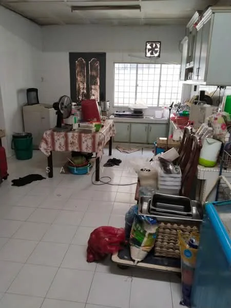 Kitchen features: white tiled flooring, white walls, kitchen cabinets with green doors, stainless-steel sink, built-in stove, table with tablecloth, plastic containers, fan, multiple kitchen appliances, cluttered countertop, window with grid pattern, various utensils and cookware.