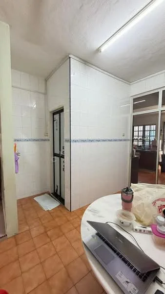Room features: white tiled walls, brown tiled flooring, built-in cabinetry, door leading to another room, round dining table, laptop on table, kitchen appliances visible, window with natural light.