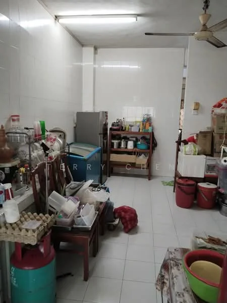 Kitchen features: white tiled walls, white tiled flooring, ceiling with fluorescent lights, 5-blade ceiling fan, wooden dining table, plastic chairs, stainless-steel fridge, multiple storage containers, gas cylinder, plastic bins, kitchen utensils, open shelving, countertop with various items.