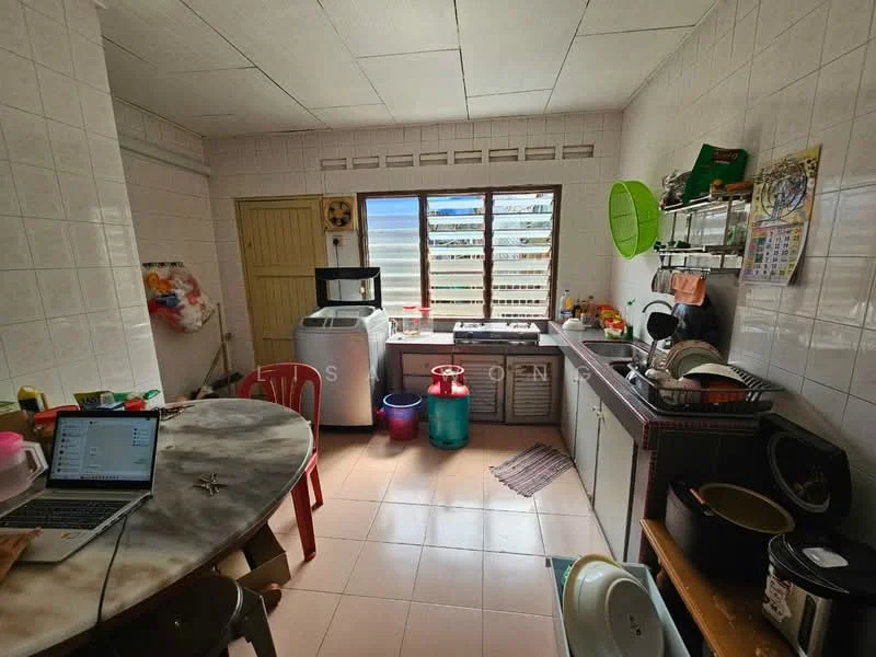Kitchen features: white tiled walls, light grey tiled flooring, single-bowl stainless-steel sink, chrome pull-down faucet, kitchen countertop with storage cabinets, built-in washing machine, window with horizontal slats, round dining table with marble top, red plastic chairs, various kitchen utensils and containers, calendar on wall, open shelving with dishes.