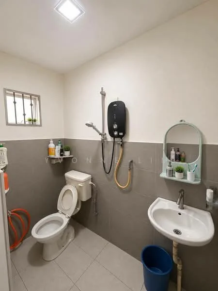 Bathroom features: white walls, grey tiled walls, grey floor tiles, one-piece toilet, wall-mounted shower with handheld showerhead, water heater, sink with wall-mounted mirror, small shelf with decorative items, window with security bars, blue waste bin; style: modern.