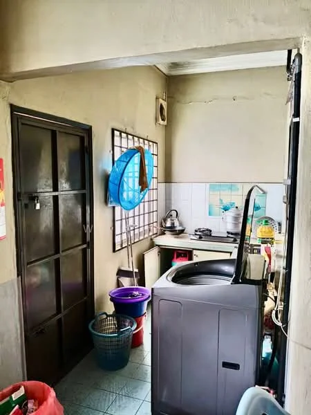 Laundry features: washing machine, grey cabinetry, white tiled walls, green tiled flooring, window with grid pattern, sink, plastic laundry basket, plastic bucket, kettle, stove, wall-mounted shelf.