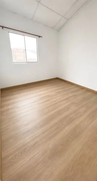 Room features: white painted walls, wooden flooring, single window, no visible furniture, high ceiling, natural light, baseboard trim, neutral color palette; style: minimalist.