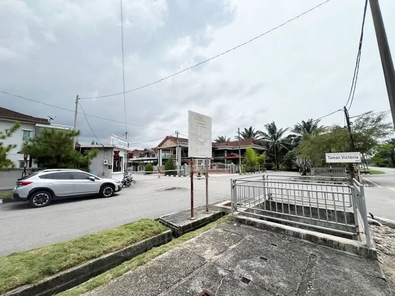 Exterior type: linked terrace house; features: residential street view, signage for Taman Victoria, paved walkway, manicured grass, surrounding palm trees, two-storey houses in background, street lighting, curbside parking, fenced property, utility poles; style: modern.